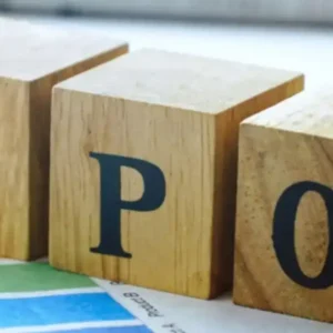 Three wooden blocks spelling "IPO" on a financial chart with a rope and blurred papers in the background.