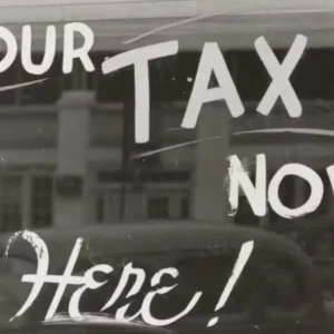 A monochrome image showing a window with "PAY YOUR TAX NOW Here!" painted on it