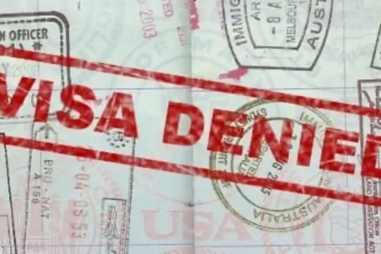 A "VISA DENIED" stamp across a passport page with various immigration stamps