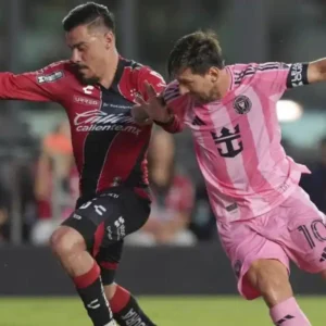 Lionel Messi in a pink jersey dribbles past a defender in a red and black jersey.