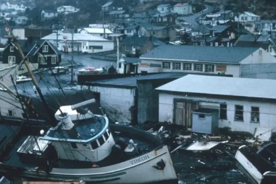 Fishing boats are beached and damaged in a coastal town after a natural disaster.