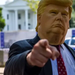 A person wearing a Donald Trump mask points, with the White House in background.