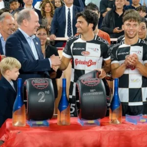 Prince Albert II of Monaco shakes hands with an athlete, surrounded by people.