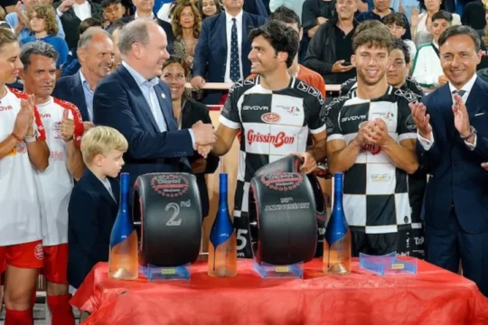 Prince Albert II of Monaco shakes hands with an athlete, surrounded by people.