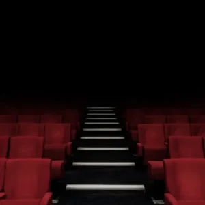 Rows of empty red seats and an aisle leading upwards in a dark theater.