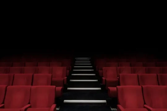 Rows of empty red seats and an aisle leading upwards in a dark theater.