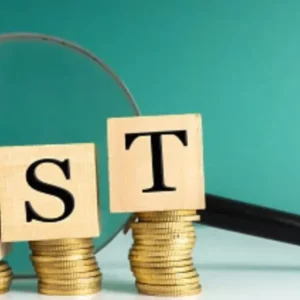 Wooden blocks spelling "GST" are stacked on coins next to a magnifying glass.