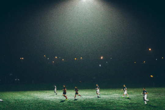 Football players on a dimly lit field under a spotlight.