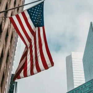 An American flag hangs from a building amidst skyscrapers in a city.