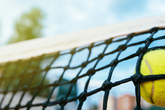 A tennis ball stuck in the net on a sunny day.