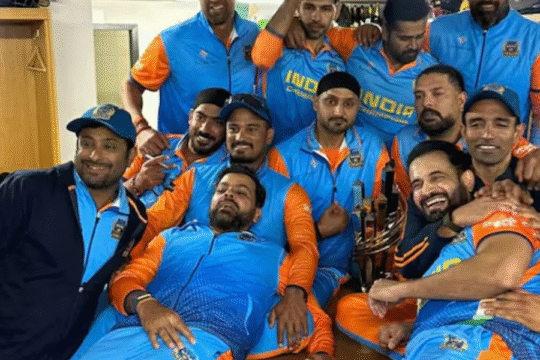 A group of male cricketers in blue and orange uniforms celebrate with a trophy in a locker room.