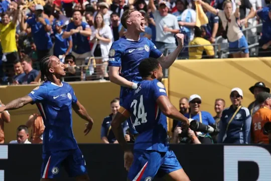 Soccer players in blue celebrating a goal in front of a cheering crowd.