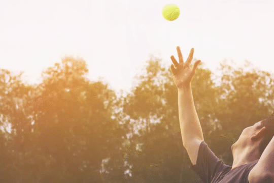 Tennis player serving, ball mid-air, with racket.