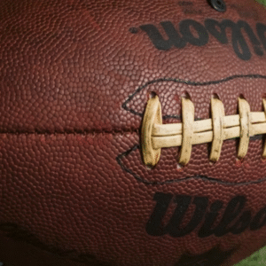 A close-up of a brown Wilson American football resting on green grass with white lines.