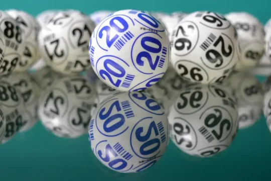 Numerous lottery balls scattered on a reflective surface, with one prominent blue "20" ball.
