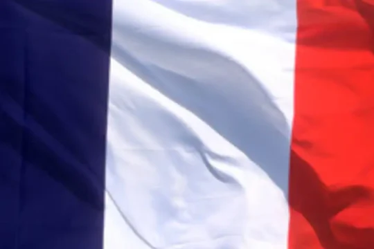 A French flag waving in the wind against a blue sky.