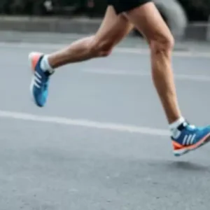 The muscular legs of a runner in blue and orange shoes in motion on pavement.