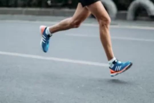 The muscular legs of a runner in blue and orange shoes in motion on pavement.