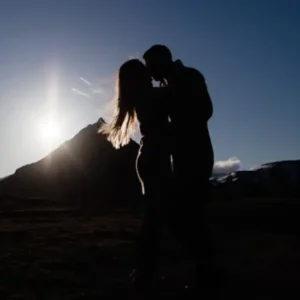 A couple silhouetted against a setting sun behind a mountain.