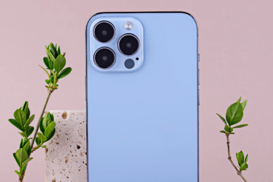 A light blue iPhone with multiple cameras, next to green leaves.
