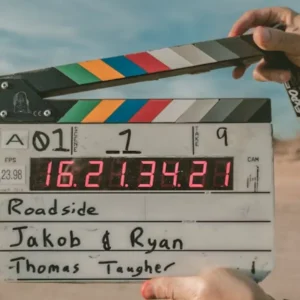 Hands hold a film clapperboard with production details against a desert background.