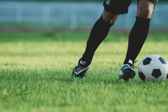 Soccer player's legs dribbling a ball on a green grass field.