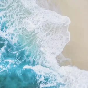 Aerial view of turquoise ocean waves meeting a sandy beach with a heart drawn in the sand.
