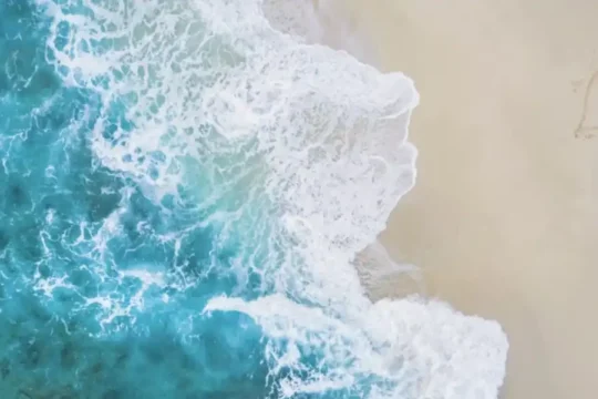 Aerial view of turquoise ocean waves meeting a sandy beach with a heart drawn in the sand.
