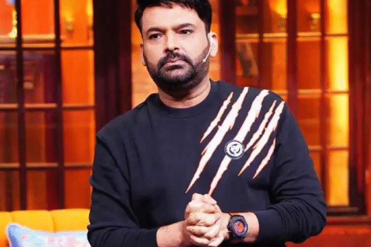 Comedian Kapil Sharma in a black sweatshirt, standing on a set.