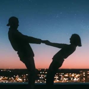 Silhouettes of two people holding hands, leaning back against a city skyline at dusk.