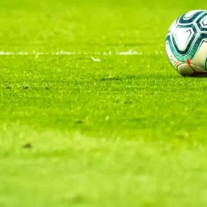 A close-up of a soccer ball and a player's foot in black cleats on a green field.