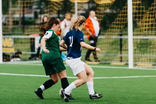 Two female soccer players in action on a green field during a game.