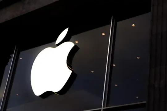 The illuminated white Apple logo on the dark exterior of an Apple Store at night.