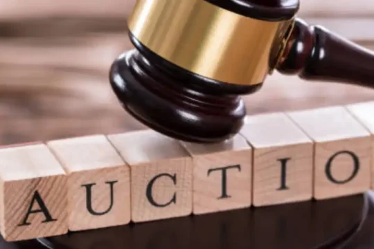 A wooden gavel rests above wooden blocks spelling out the word "AUCTION."