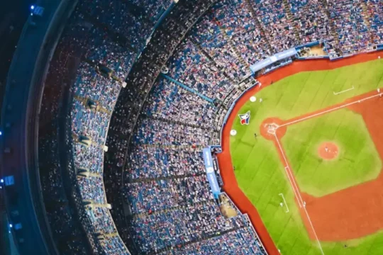 An aerial view of a packed baseball stadium with a green field and red dirt infield.