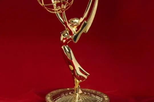 A close-up of a golden Emmy Award statue standing on a dark base against a rich red background.