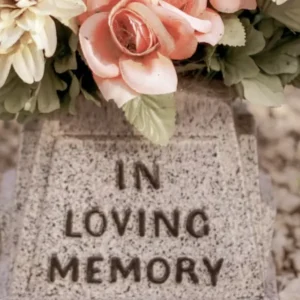 A stone vase with "IN LOVING MEMORY" inscribed, holding pink, peach, and yellow flowers.