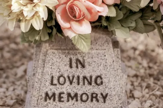 A stone vase with "IN LOVING MEMORY" inscribed, holding pink, peach, and yellow flowers.