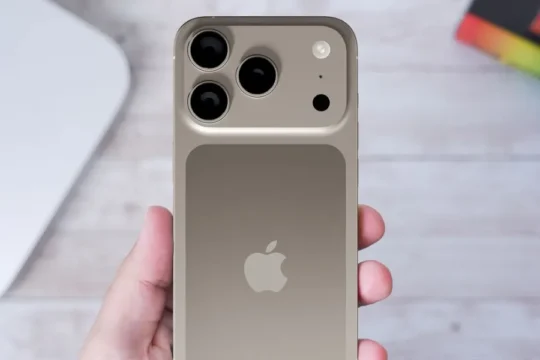 A hand holds a gold iPhone with multiple cameras, Apple logo visible.