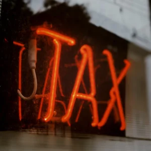 Neon sign glowing in red with the word "TAX" reflected on a glass window.