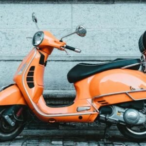 Bright orange electric scooter parked against a stone wall, symbolizing eco-friendly urban transport.