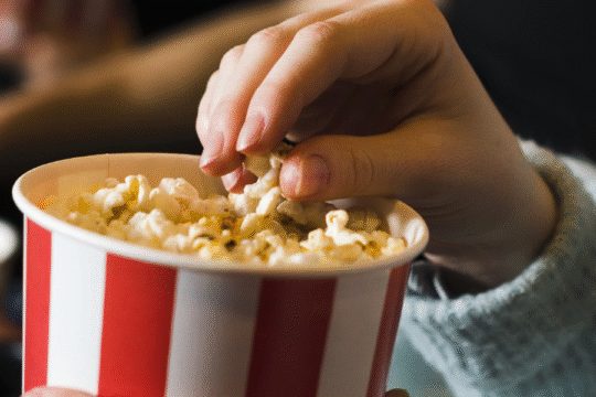 Hand picking popcorn from striped tub at theater