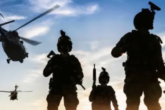 Silhouetted soldiers with rifles and helicopters flying in the background during a military operation at sunset.
