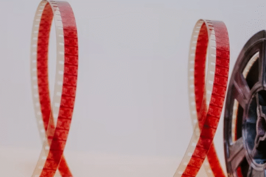Close-up of vintage film reel with red film strip unspooled on white background