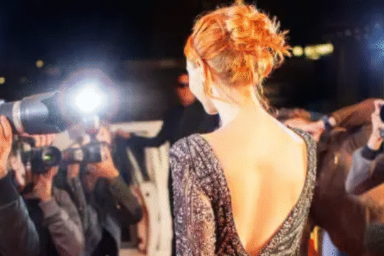 Female celebrity posing on red carpet as paparazzi take photos with flashing cameras