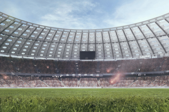 Wide-angle view of a packed football stadium under a clear sky, with green grass and spectators ready for an intense soccer match.