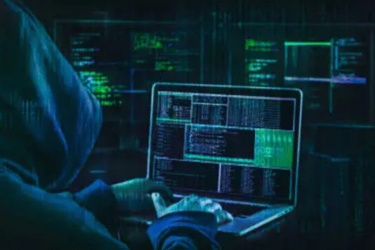 Hacker in hoodie using laptop with multiple digital code screens
