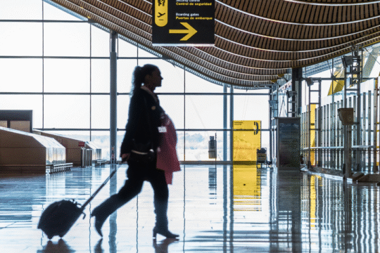 Traveler walking through modern airport terminal with luggage and security signs