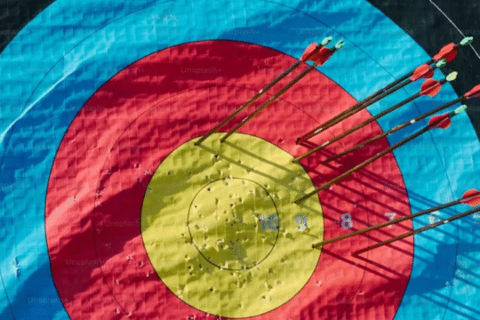 A close-up of an archery target with multiple arrows striking various rings, symbolizing precision, focus, and competition.