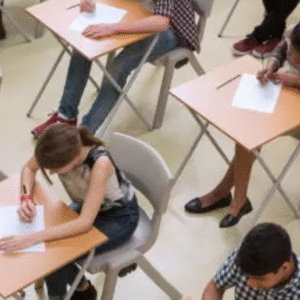 Students sitting in an exam hall writing answers on desks during a test.